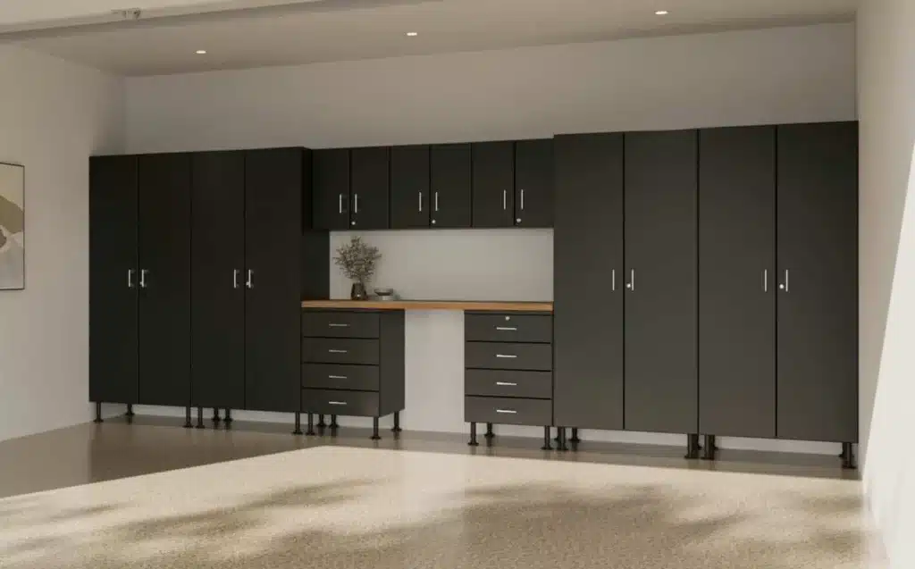 A modern, clean garage interior with dark gray storage cabinets, a light wood countertop, and a well-lit, spacious area. A single plant decorates the space.