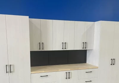 The image shows a modern kitchen cabinet wall with light wood finishes, black backsplash, and silver handles set against a blue wall.