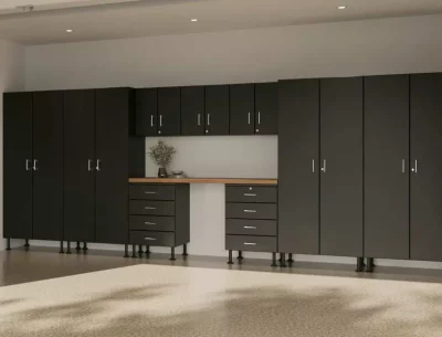 A modern, clean garage interior with dark gray storage cabinets, a light wood countertop, and a well-lit, spacious area. A single plant decorates the space.